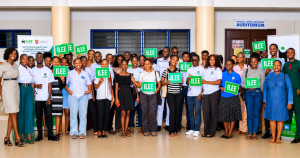 Group photo of ILEE participants and organizers holding ILEE signs at the University of Cape Coast auditorium after an entrepreneurship and economic education event.