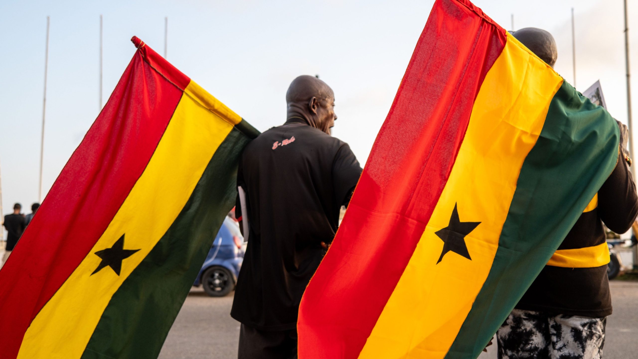 Two people carry large Ghanaian flags outdoors.